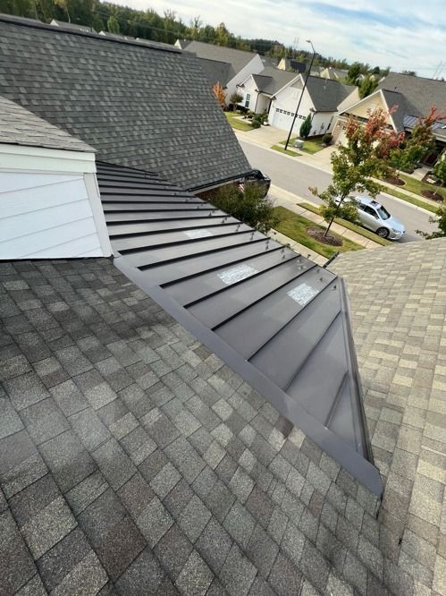 Rooftop with dark gray shingles and metal siding extension overlooking a suburban neighborhood