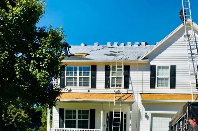 White two-story house with black shutters, yellow trim, and a ladder under a blue sky