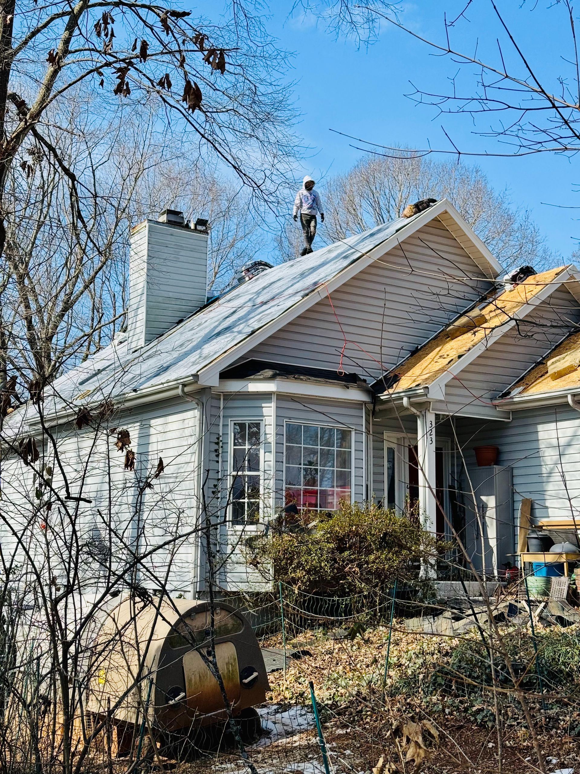 Small white house with a steep roof, bare trees, and a person standing on the roof.