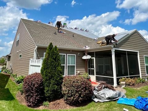 Roofers working on a tan house roof with shingles and tools in the yard