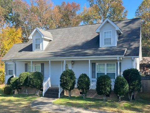 White house with gray roof, front porch, and trimmed bushes in a sunny yard with autumn trees.