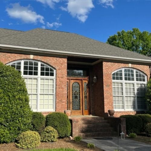 Brick house front entrance with arched windows, wooden double doors, and manicured shrubs under a blue sky