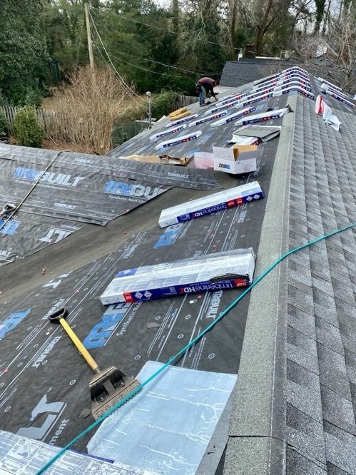 Roof under repair with shingles, tools, and a worker near the ridge line