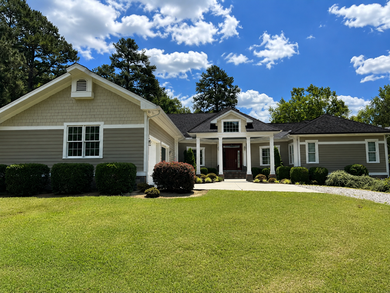 Single-story beige house with white trim, front porch, and a green lawn under a blue sky.