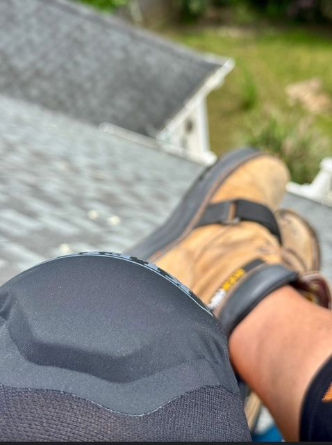 Feet in tan hiking shoes resting on a roof edge, overlooking a blurred green yard.