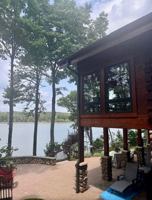 Lakefront cabin porch with stone columns, trees, and a lake view at sunset