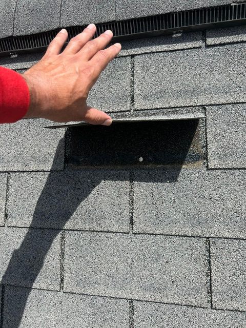 Hand reaching toward a black roof vent on gray asphalt shingles