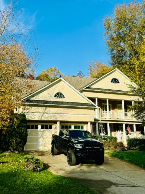 Black SUV parked in front of a two-story cream house with a porch and autumn trees