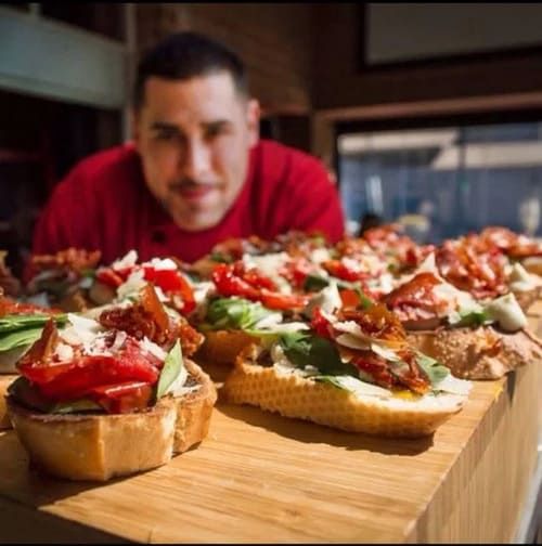 Bruschetta on a wooden board with a blurred person in a red shirt in the background
