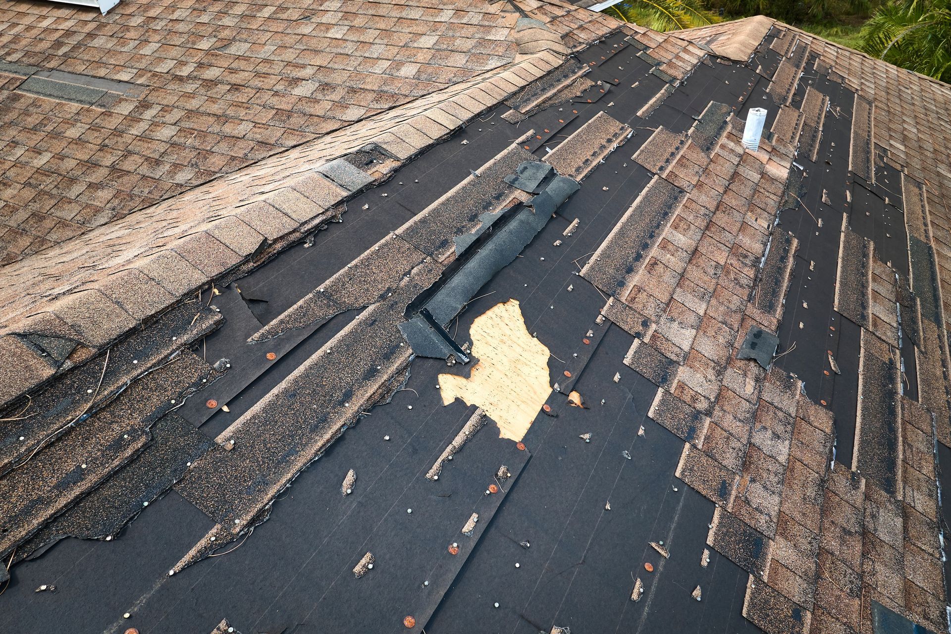Damaged roof with torn black shingles and exposed underlayment near a tan shingle section