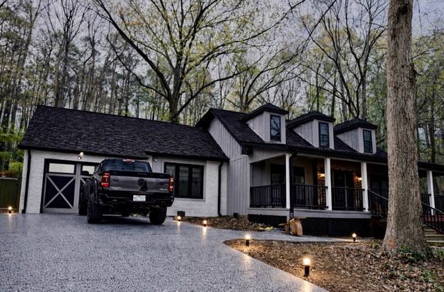 Black pickup in gravel driveway beside modern house and garage, with lit path lights at dusk