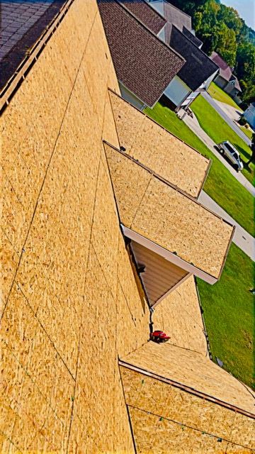 Diagonal view of a tan shingle roof with dormers and green lawns beside it under sunny skies