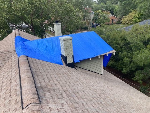 Roof damaged and covered with a bright blue tarp, viewed from above among trees.