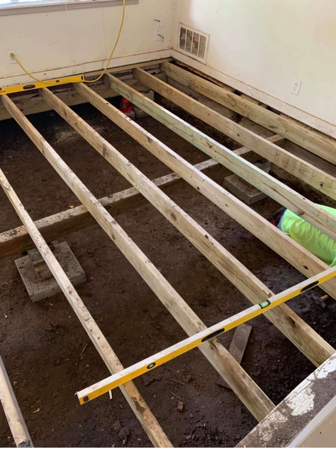 Partially demolished room floor with exposed joists and a yellow level across the framing