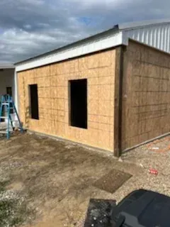Partially finished tan house with black window openings and a ladder outside under a cloudy sky