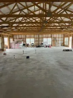 Large unfinished wooden building interior with exposed trusses and a concrete floor.