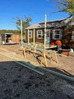 Outdoor construction site with workers installing wooden framing beside a small building under a blue sky