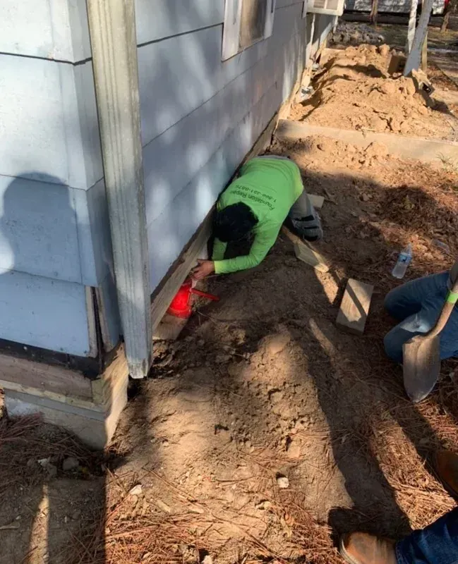 Workers digging a trench beside a house foundation during exterior repairs.
