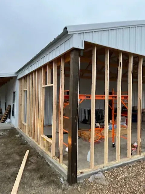 Partially framed addition to a metal building under construction, with exposed studs and open doorway