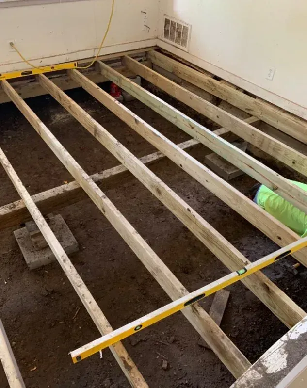 Exposed floor joists in a room under renovation, with a yellow level laid across them.