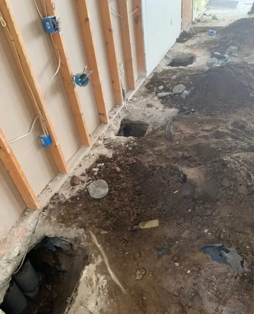 Damaged floor with holes and exposed studs along a wall in an unfinished interior.