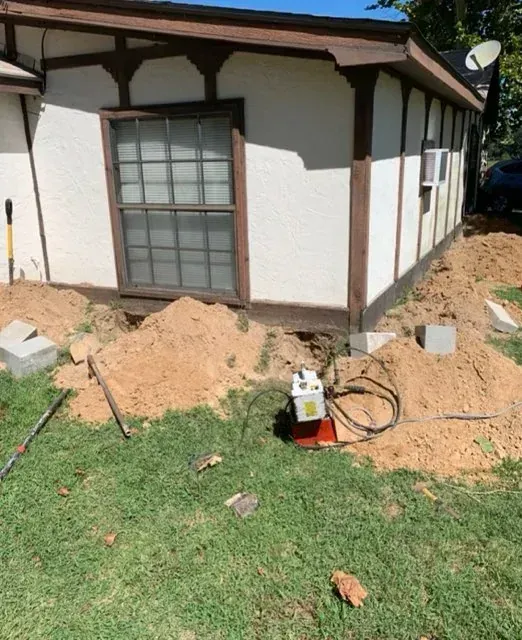 House exterior with dug-up soil and construction tools along the foundation and lawn