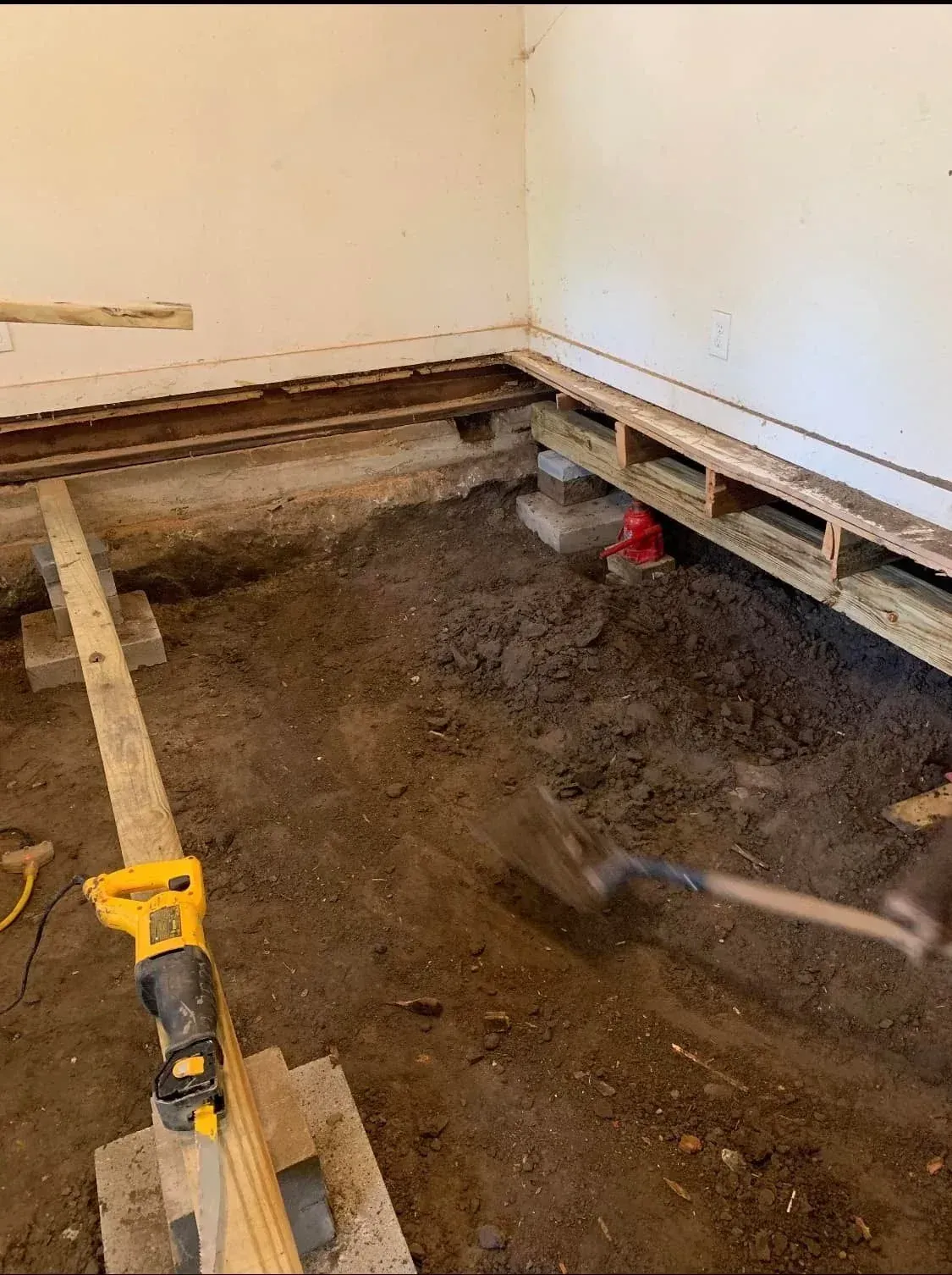 Crawlspace floor under renovation with exposed dirt, open joists, and a yellow tool in the foreground