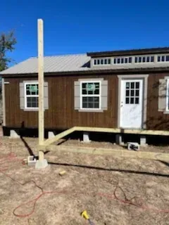 Small brown house with white trim and porch under construction, with a tall post in the foreground.