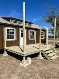Small wooden cabin with porch posts and steps on a dirt lot under a blue sky