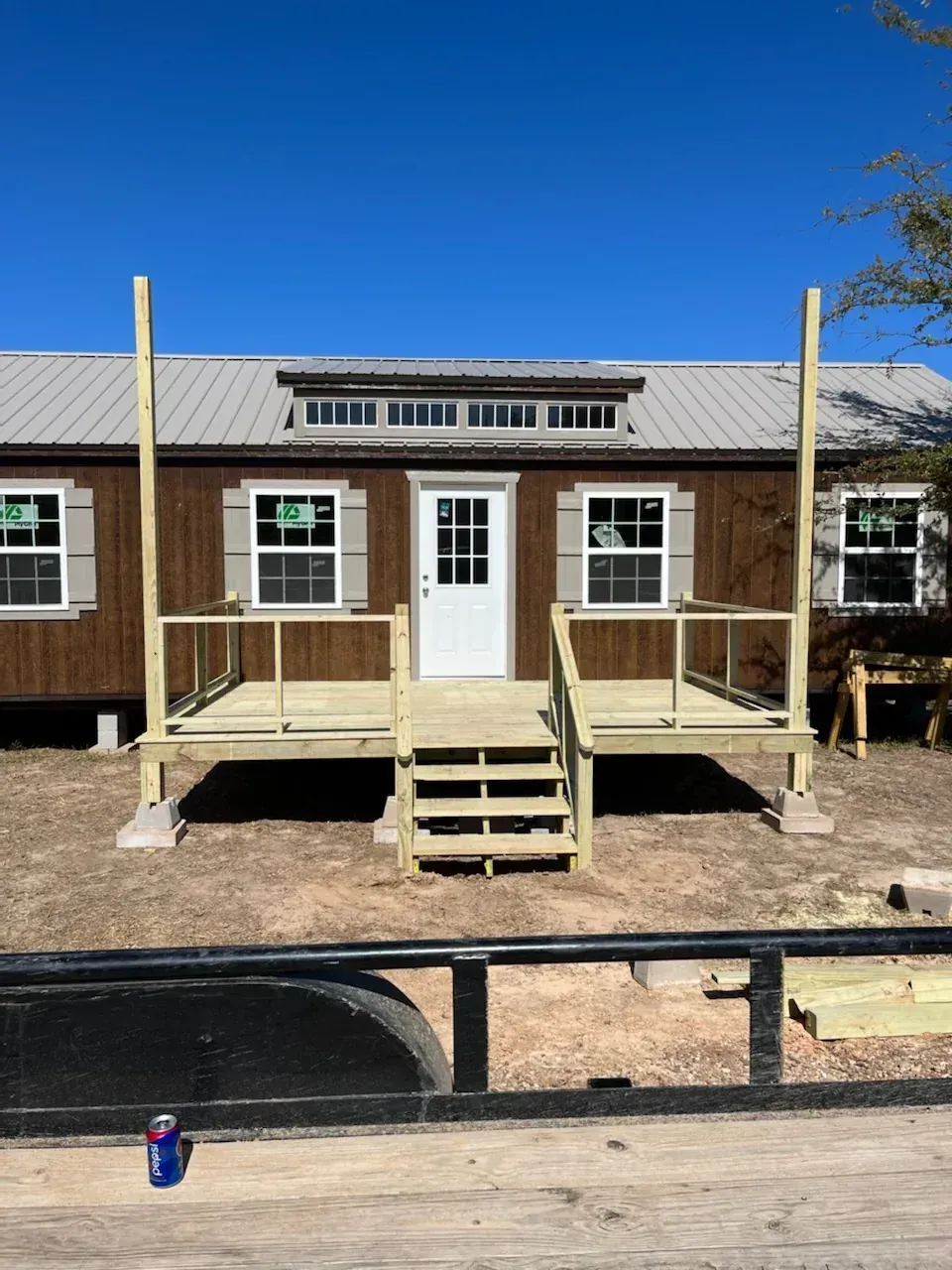 Brown building with a white door and porch steps, framed by a black fence under a clear blue sky.