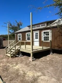 Wooden porch ramp with posts on a small brown house under a clear blue sky