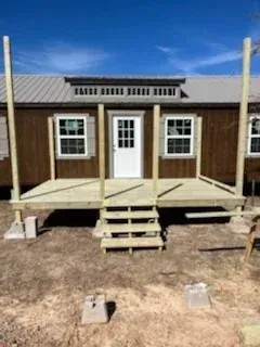 Small wooden house porch with steps, white door, and windows under a blue sky.