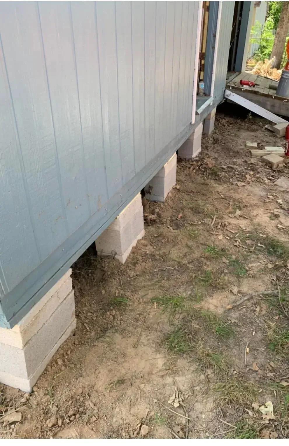Raised mobile home on cinder blocks beside patchy dirt yard and walkway
