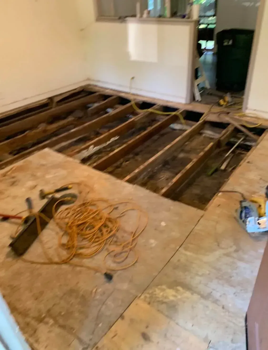 Interior room under renovation with exposed floor joists, tools, and wiring on the subfloor.