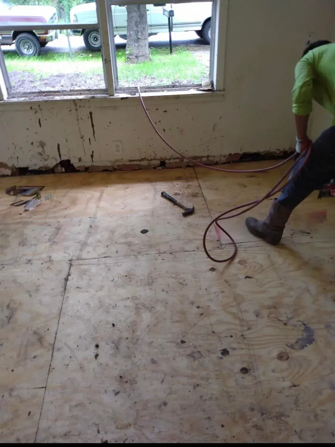 Person using a floor sander on a bare room floor near a window.