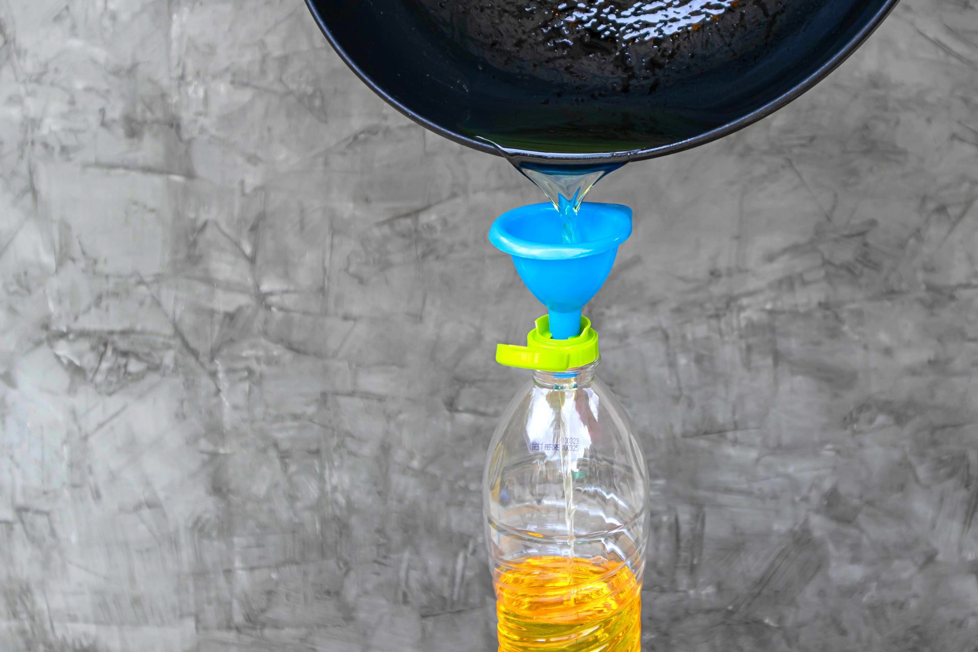 Pouring used cooking oil from the pan into a plastic bottle.
