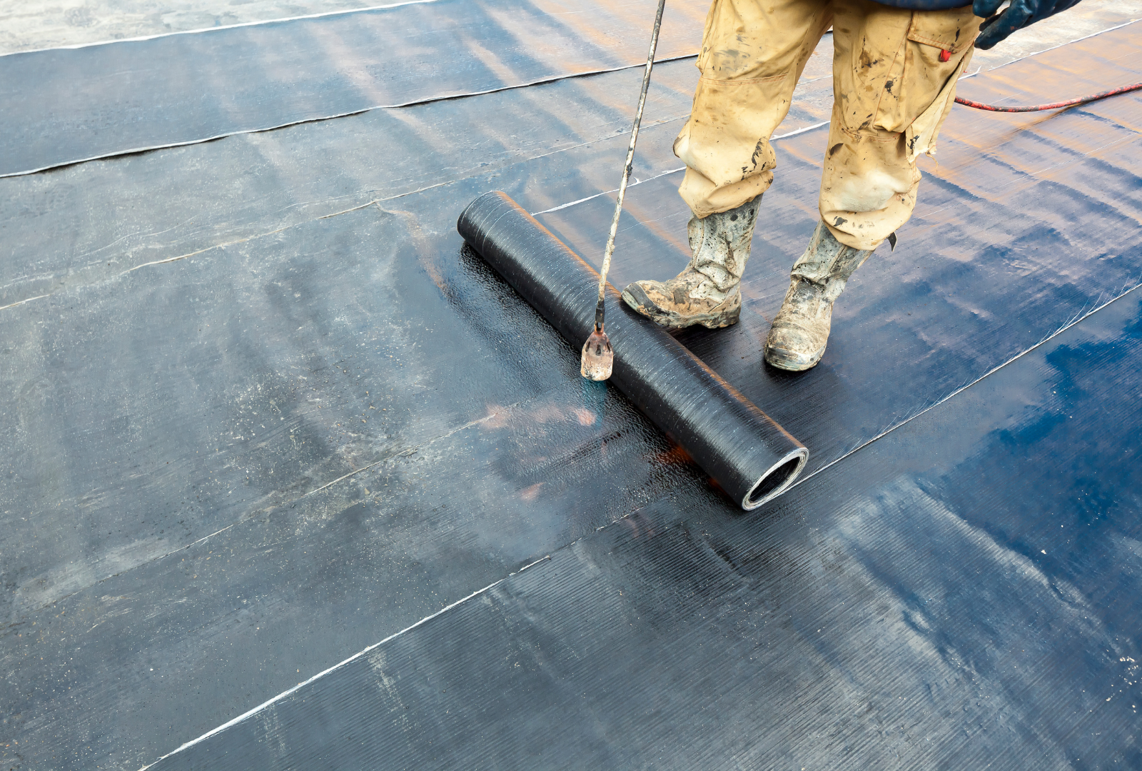 Person using a torch to install a black roofing membrane.