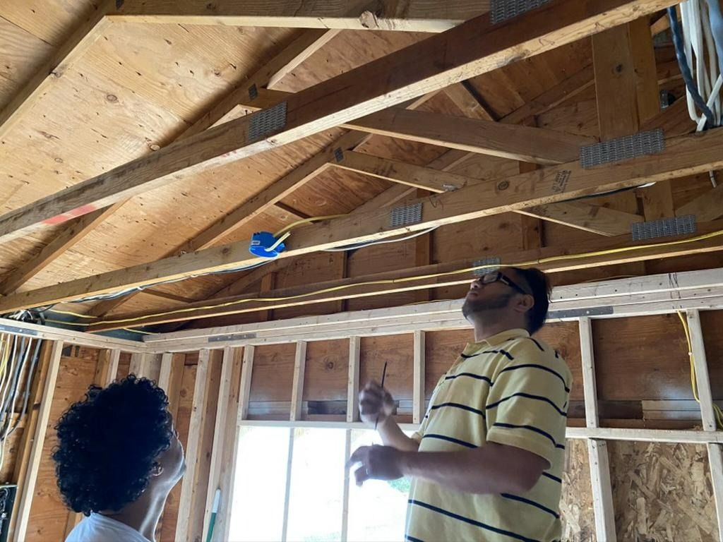 Two men are looking up at the ceiling of a house under construction.