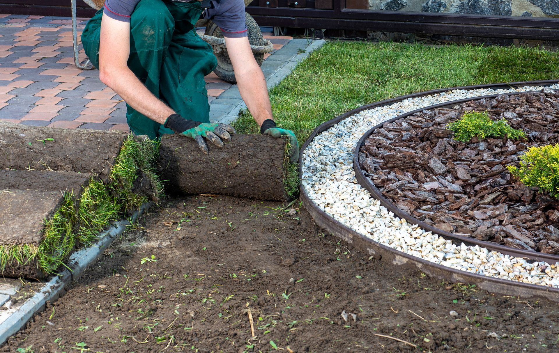 A man is laying a roll of turf in a garden.