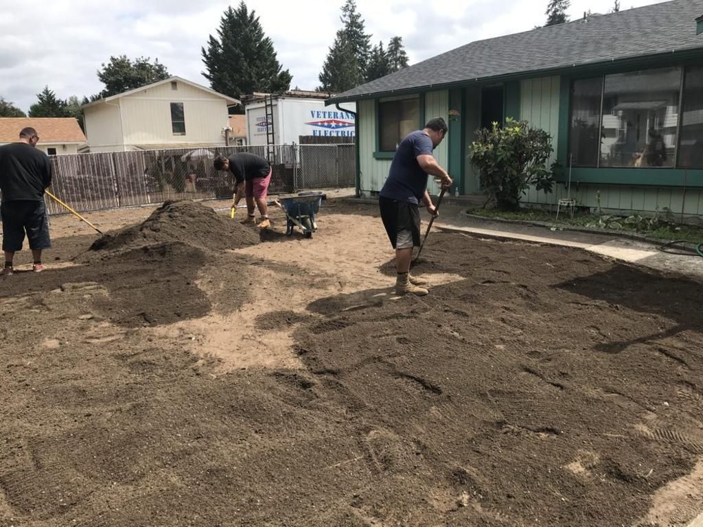 A group of people are working on a dirt yard in front of a house.
