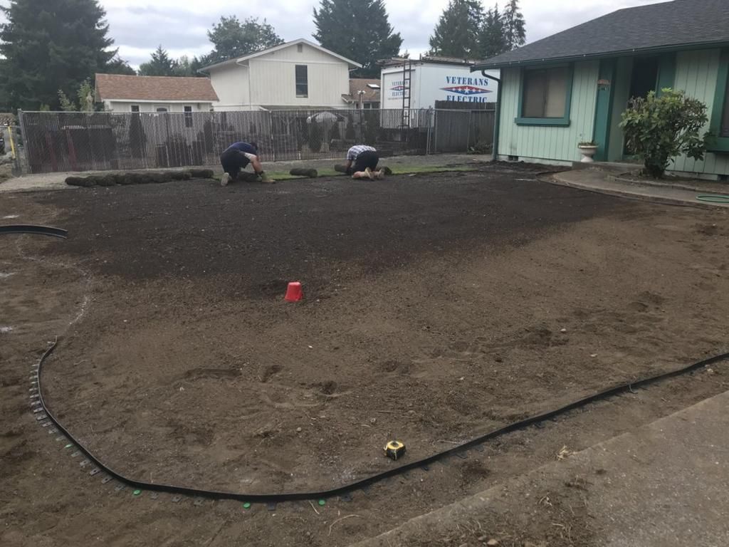 Two people are working on a lawn in front of a house.