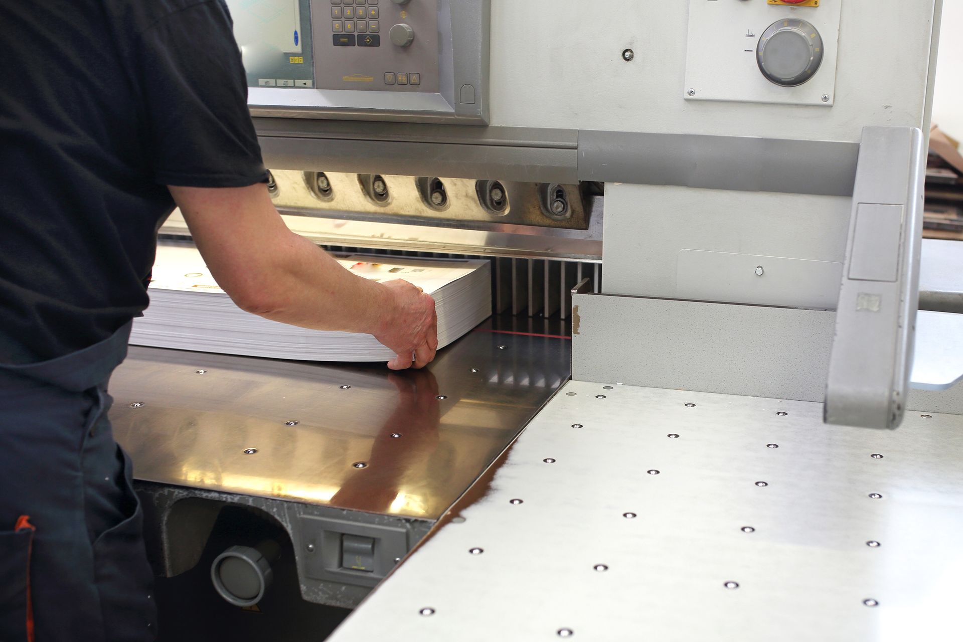 A person using a professional paper guillotine machine to trim a large stack of paper.