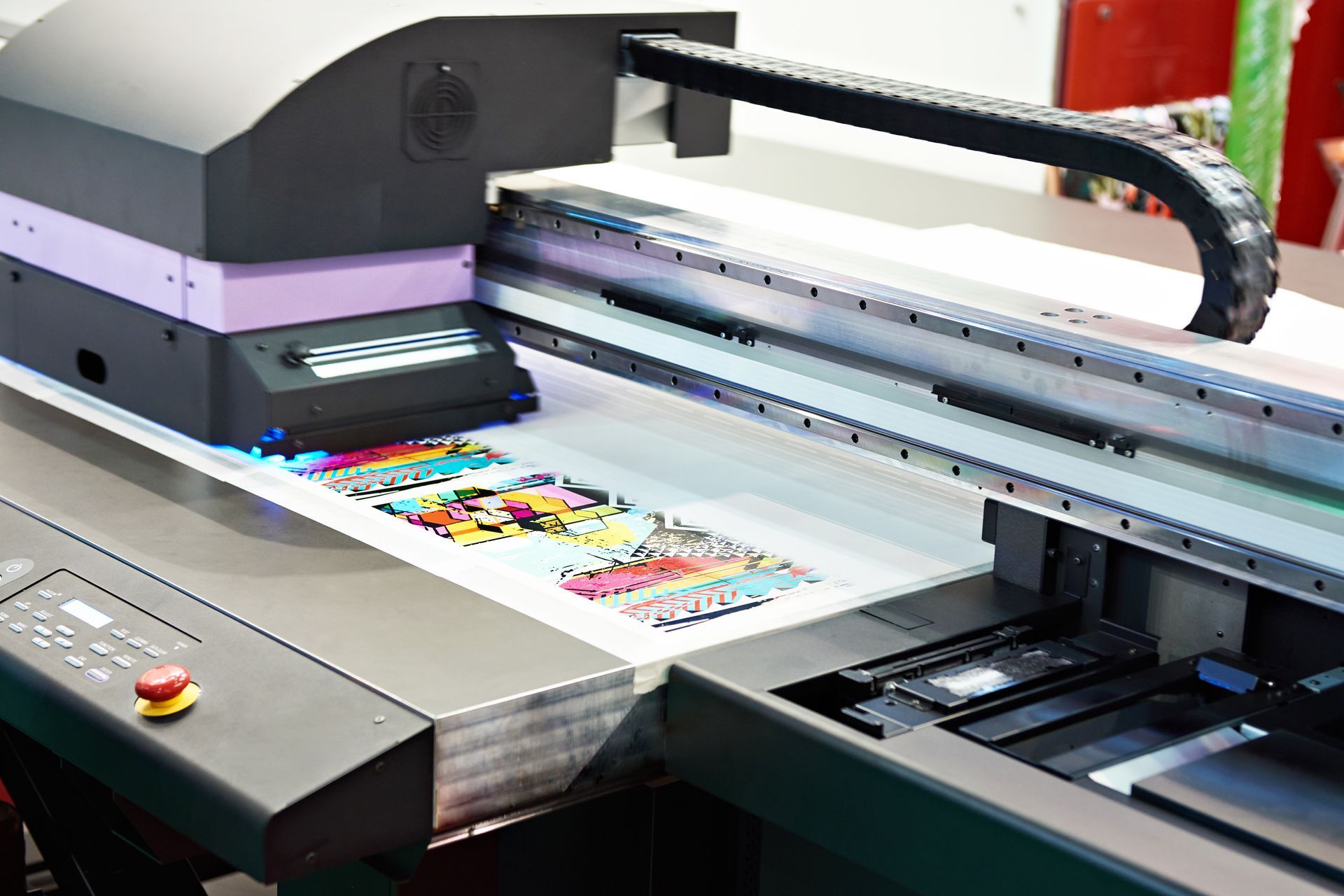 A large format flatbed industrial printer printing colorful graphics onto a white substrate.