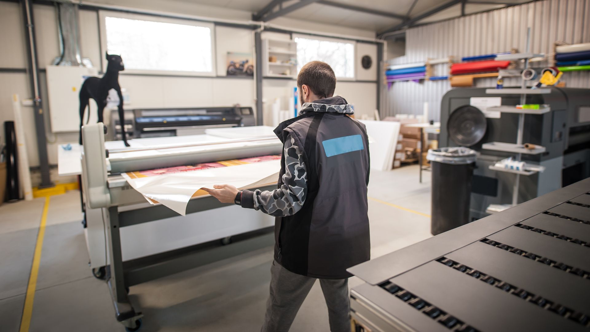A worker in a shop loads a printed roll into a large format industrial printer.