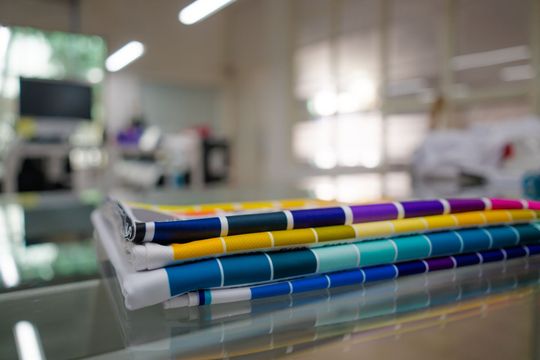 A stack of colorful Pantone color swatch books lying on a glass table in a bright, blurred workshop.