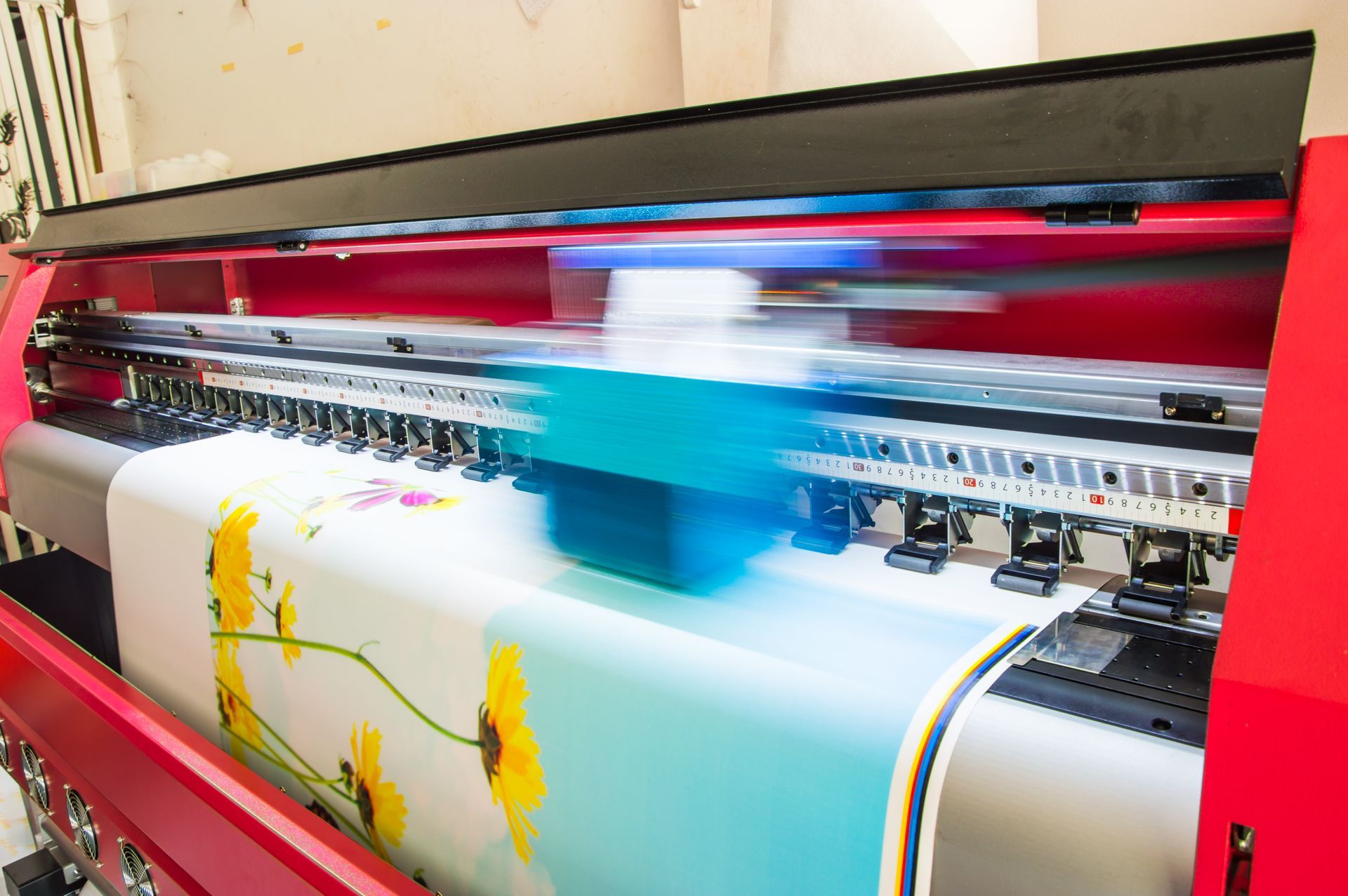 A large-format digital printer in action, printing a colorful graphic of yellow flowers onto a white material.