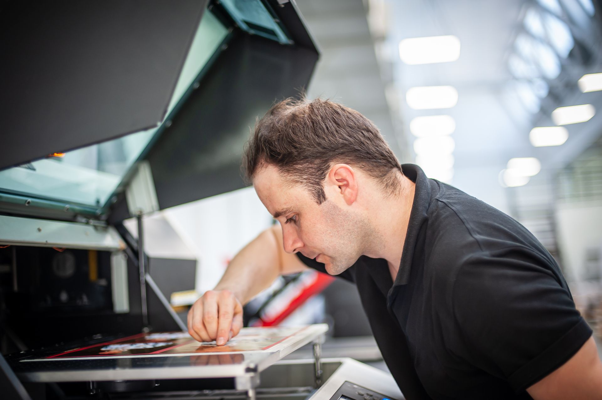 A person in a black polo shirt carefully adjusting materials inside a commercial printing machine.