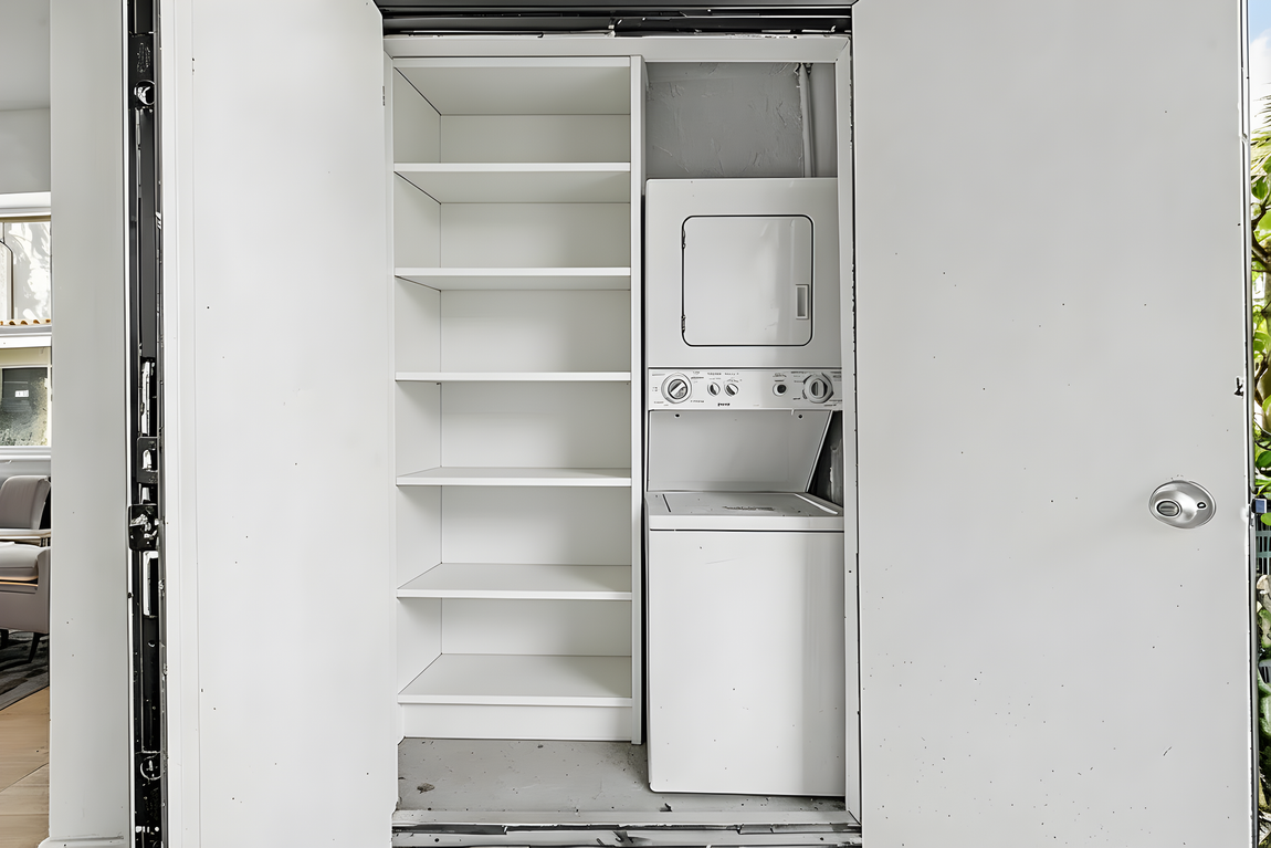 A closet containing white shelving next to a stacked white washer and dryer unit.