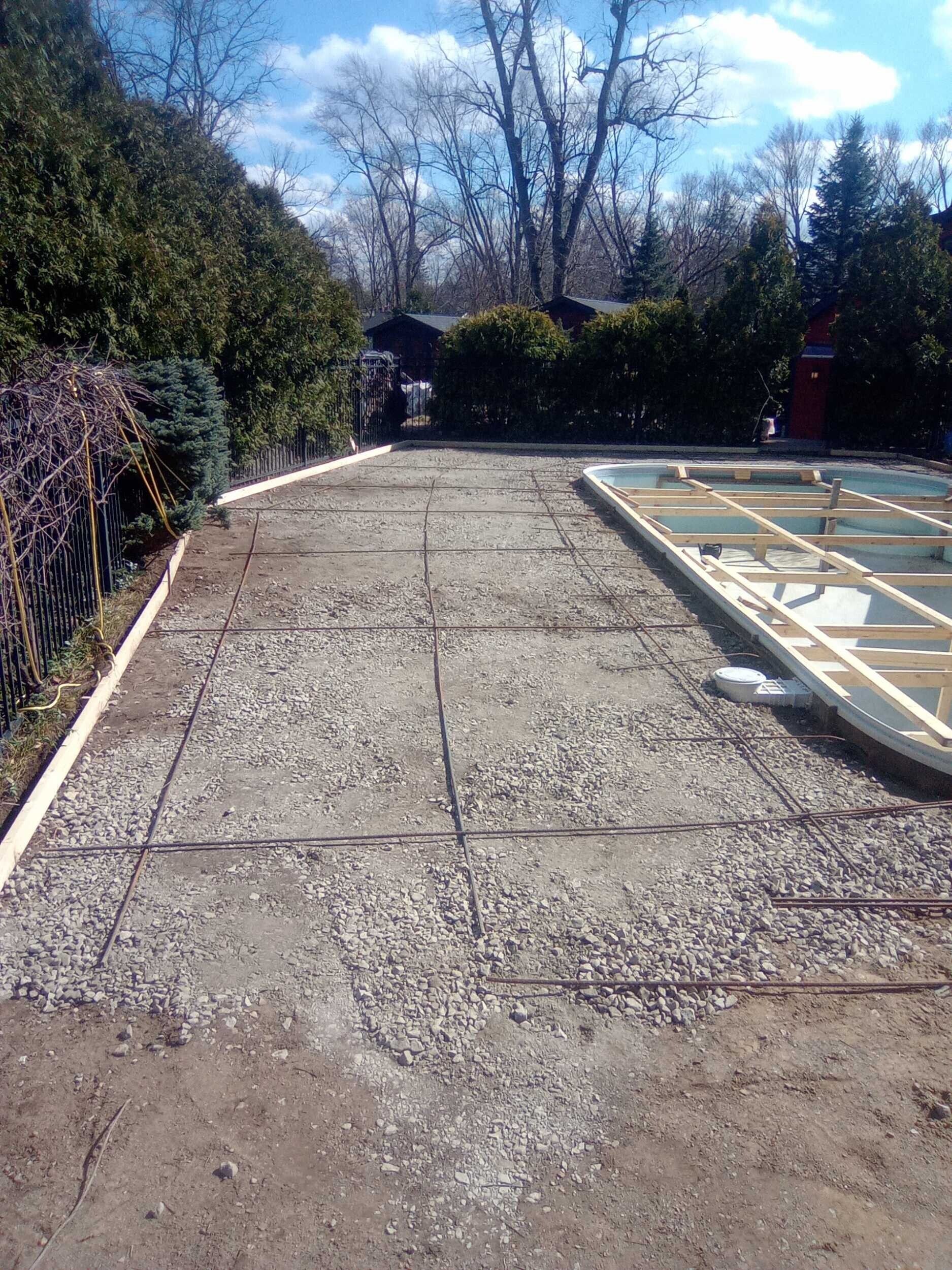 Gravel driveway beside a covered pool frame, lined with hedges and trees under a clear blue sky