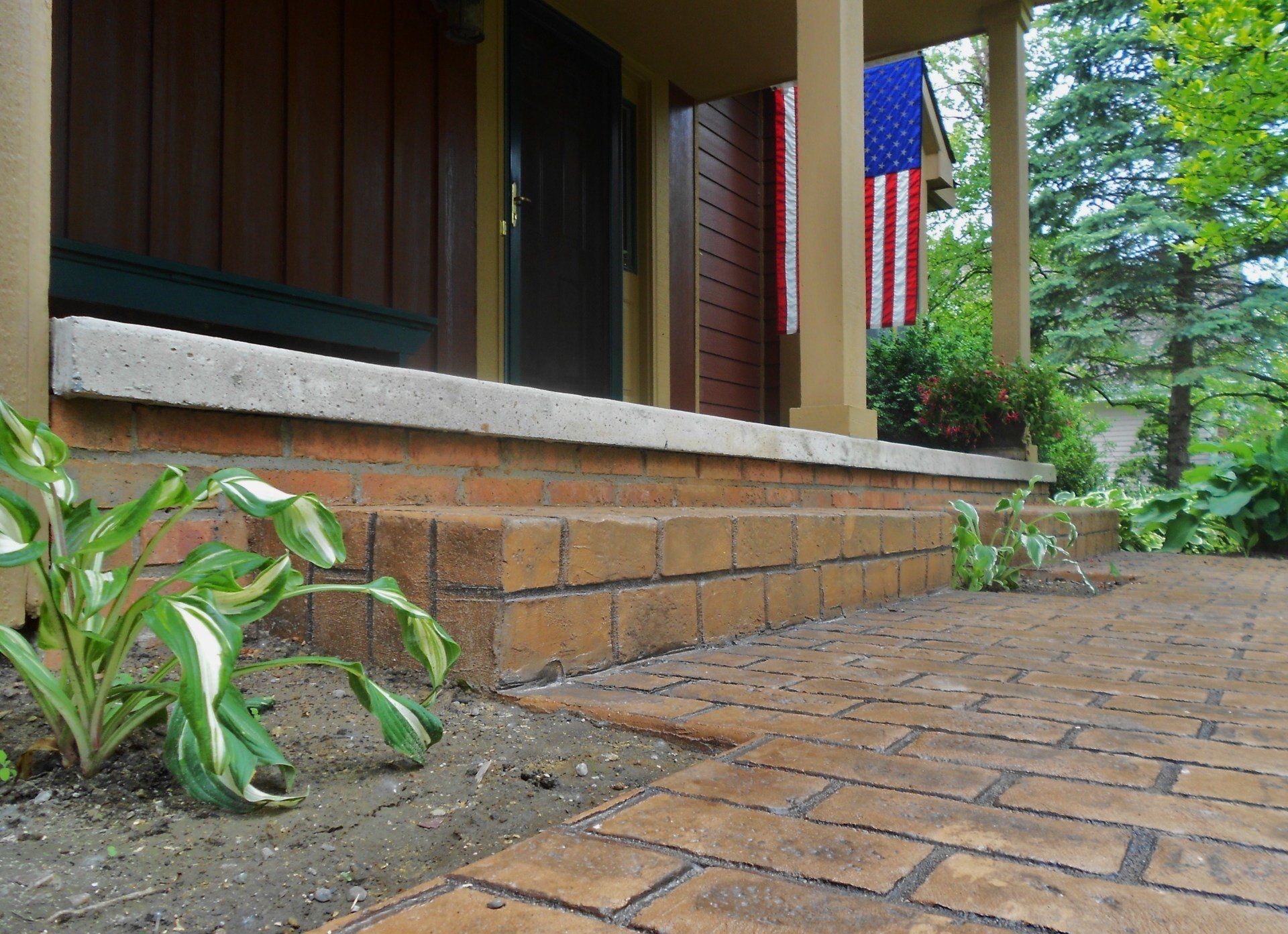 Brick patio beside a porch with an American flag and green plants